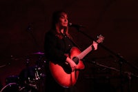 a woman playing an acoustic guitar in front of a microphone