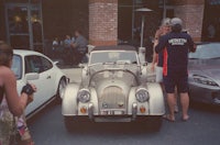 a group of people posing for a picture in front of a classic car