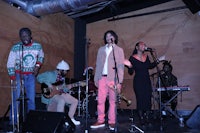 a group of people singing on stage in front of a wooden wall